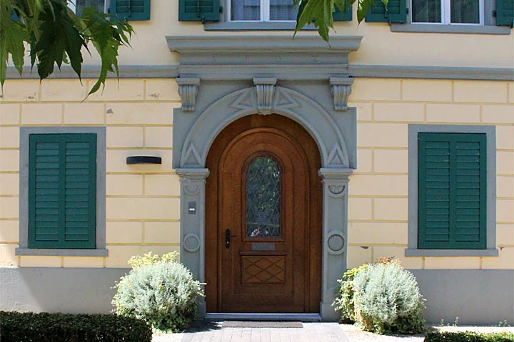 Eingang zur Gesundheitspraxis Monika Imhof in Altdorf mit Holztür und grünen Fensterläden